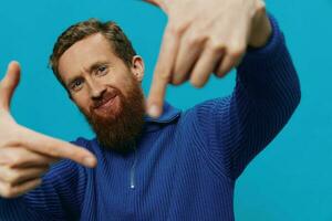 Portrait of a man in a sweater smile and happiness, hand signs and symbols, on a blue background. Lifestyle positive, copy place. photo