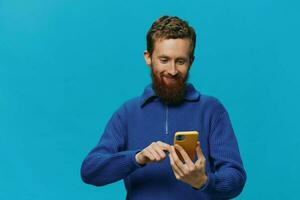 Portrait of a man with a phone in his hands does looking at it and talking on the phone, on a blue background. Communicating online social media, lifestyle photo