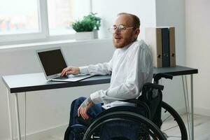 un hombre silla de ruedas, empresario en el oficina trabajando computadora portátil, trabajando en línea, social redes puesta en marcha, integración dentro sociedad, el concepto de trabajando un persona con discapacidades, un real persona de cerca foto