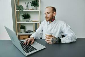 A man in a wheelchair, a businessman with tattoos in the office at a laptop, a coffee break, annoyance, the concept of working a person with disabilities, freedom from social frames photo