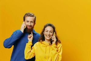 Man and woman couple smiling merrily with phone in hand social media viewing photos and videos, on yellow background, symbols signs and hand gestures, family freelancers.