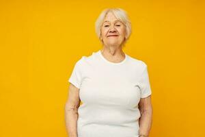 elderly woman in casual t-shirt gestures with his hands yellow background photo