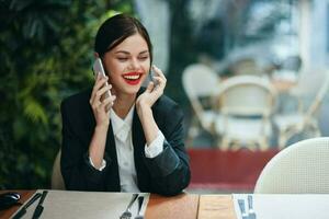woman blogger tourist sits in a cafe at a table with a phone in her hands talking on the phone, mobile communications and the Internet on a spring trip, video call, freelance work online, smile photo