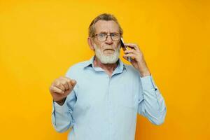 retrato de contento mayor hombre gris barba con lentes hablando en el teléfono amarillo antecedentes foto