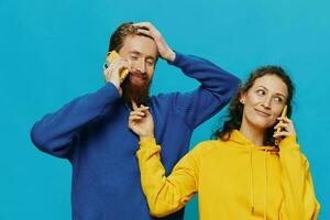 mujer y hombre alegre Pareja con Los telefonos en su manos torcido sonrisa alegre, en azul antecedentes. el concepto de real familia relaciones, hablando en el teléfono, trabajo en línea. foto