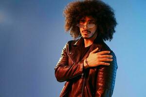 Portrait of a stylish man with curly hair on a blue background multinational, colored light, trendy glasses, modern concept. photo