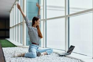 A woman freelancer sits in the office lobby by the big windows with a laptop online via the Internet, freelance work anywhere in the world photo