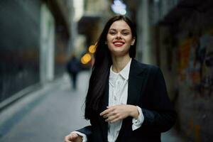 Fashion woman smile with teeth portrait tourist in stylish clothes in jacket with red lips walking down narrow city street flying hair, travel, French style, cinematic color, retro vintage style. photo