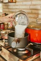 Chef pours sugar into pot on the gas stove photo