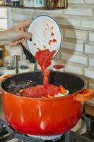 Chef adds tomato paste to the pot of ingredients on the gas stove photo