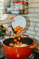 Chef adds sliced carrots to the pot with the ingredients on the gas stove photo