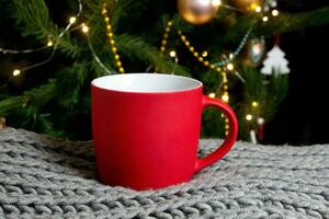 taza roja en blanco con árbol de navidad en el fondo, taza de té o café con decoración de navidad y año nuevo, maqueta horizontal con taza de cerámica para bebidas calientes, plantilla de impresión de regalo vacía. foto