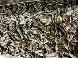 Close view of Kuaci or kwatji sunflower seeds. Scattered on a wooden table. Snack on dried and salted sunflower seeds. Selective focus photo