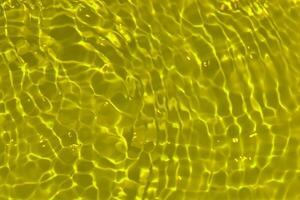 Yellow water with ripples on the surface. Defocus blurred transparent gold colored clear calm water surface texture with splashes and bubbles. Water waves with shining pattern texture background. photo