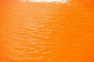 naranja agua con ondas en el superficie. desenfocar borroso transparente amarillo de colores claro calma agua superficie textura con salpicaduras y burbujas agua olas con brillante modelo textura antecedentes. foto