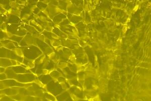 Yellow water with ripples on the surface. Defocus blurred transparent gold colored clear calm water surface texture with splashes and bubbles. Water waves with shining pattern texture background. photo