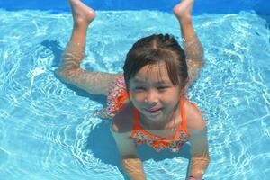 contento pequeño niña nadando piscina en un caliente verano día. niños aprender a nadar. niño agua juguetes niños jugar en tropical centros turísticos familia playa vacaciones. foto