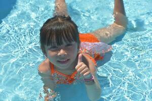 contento pequeño niña nadando piscina en un caliente verano día. niños aprender a nadar. niño agua juguetes niños jugar en tropical centros turísticos familia playa vacaciones. foto