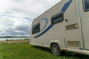 Camper trailer for traveling standing on shore of the lake in summer photo