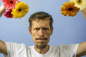 un enojado, irritado hombre en un blanco camiseta batidos y columpios flores foto