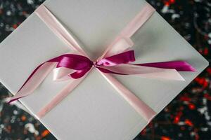 white gift box tied with a red ribbon on a spotted colored background photo