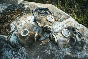 three old used gas masks are lying on a large boulder in the forest photo