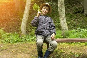 funny Caucasian boy in a traveler's hat and windbreaker sits on a bench photo