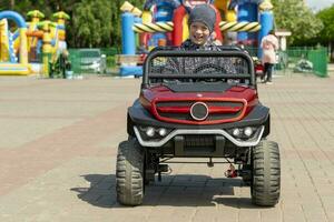 alegre contento sonriente chico paseos un para niños eléctrico coche en el parque foto