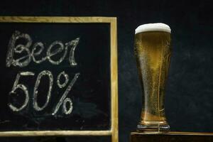 A glass of fresh and cold beer on a wooden table on a dark background. photo