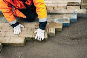 a worker in a protective work suit lays paving slabs. A professional photo