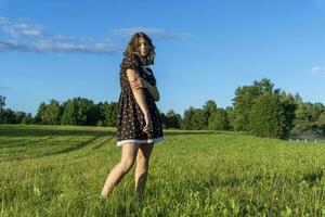 Beautiful girl in a short dress on the background of a green field in summer in the setting sun photo