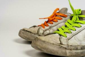 worn old torn white sneakers with colored laces on a white background photo