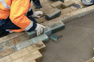 a worker in a protective work suit lays paving slabs. A professional photo