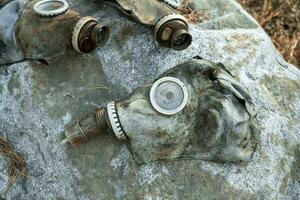 three old used gas masks are lying on a large boulder in the forest photo