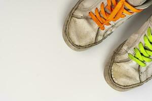 worn old torn white sneakers with colored laces on a white background photo