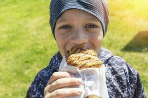 a cheerful cheerful boy is eating a bun on the street photo
