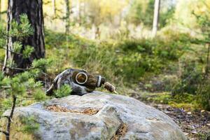 old used gas mask is lying on a large boulder in the forest photo