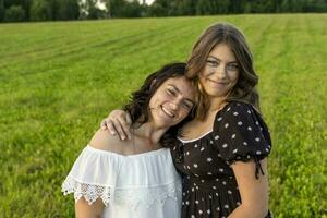 contento mamá abrazos su Adolescente hija en contra un verde campo foto