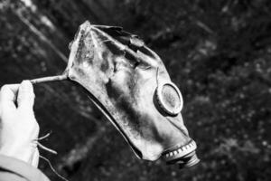 an old used gas mask in the hand of a man in the forest photo