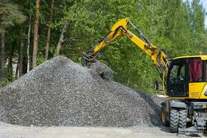 excavator takes a bucket of crushed stone from a large pile of rubble photo