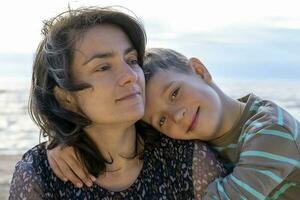 Cute happy boy hugs his mom by the sea. looking into the camera photo