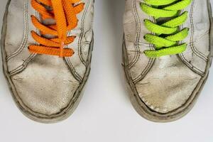 worn old torn white sneakers with colored laces on a white background photo