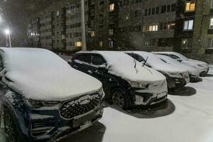 Snow-covered cars parked in a row in an open parking lot in the yard photo