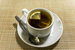 un elegante blanco taza de té con un rebanada de limón en el mesa foto