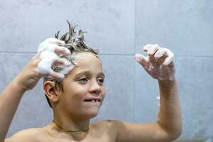 A happy boy washes his head in the bathroom with shampoo photo