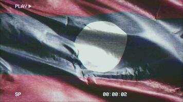 VHS video casette record Laos flag waving on the wind. Glitch noise with time counter recording Laotian banner swaying on the breeze. Seamless loop.