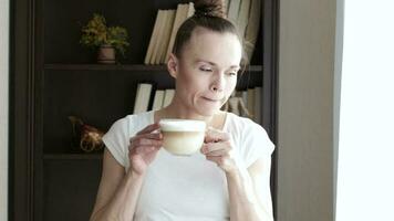 jong dame is in haar kantoor Bij huis drinken koffie terwijl kijken uit de venster video