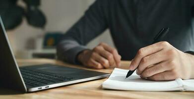 left handed man writes in a notebook on the table with laptop computer, Businessman. photo