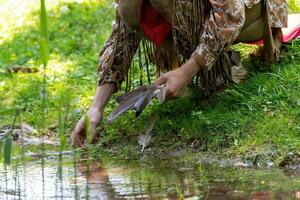 Man picks up a bird's feather in a meadow on the banks of a stream photo