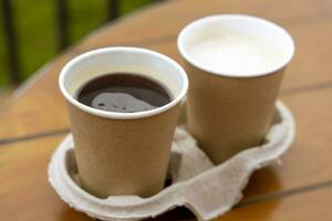 papel tazas con café en el mesa de un al aire libre cafetería. para llevar alimento. foto